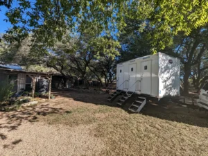 White 3-stall restroom trailer set up under oak trees at a Hill Country venue