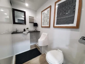 Men's side of a restroom trailer with toilet, urinal and vanity sink
