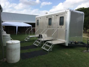 Silver three-door restroom trailer set up on grass at a ranch event